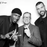 Three men pose before a white backdrop with An Evening of Music and nn Foundation logos; two make peace signs, center wears glasses.